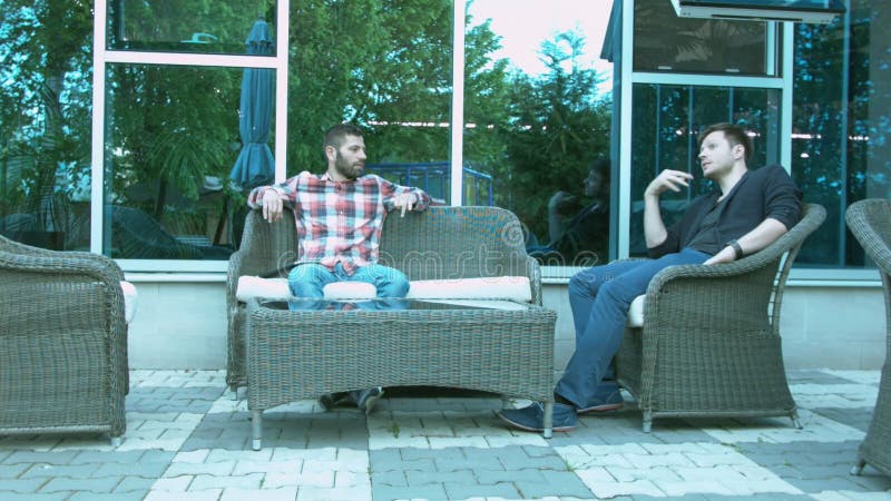 Dois homens discutem o negócio que senta-se em cadeiras de vime fora no restaurante
