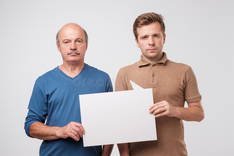 Dois homens maduros genam e o filho está mantendo um quadro de avisos vazio branco unido fotografia de stock royalty free Dois homens maduros genam e o filho está mantendo um quadro de avisos vazio branco unido fotografia de stock royalty free