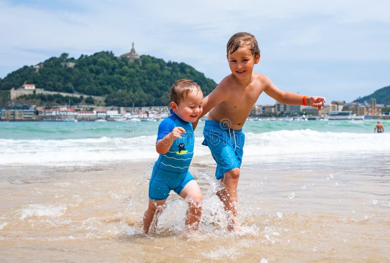 Dois meninos felizes na corrida ao longo de uma praia que faz grande espirram imagens de stock royalty free Dois meninos felizes na corrida ao longo de uma praia que faz grande espirram imagens de stock royalty free
