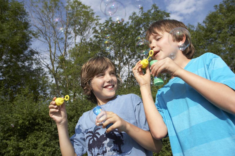 Dois meninos que fundem bolhas de sabão no parque foto de stock Dois meninos que fundem bolhas de sabão no parque foto de stock