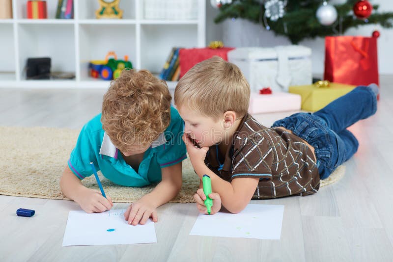Dois meninos tiram Santa Claus no papel no assoalho no berçário Caixas com os presentes sob a árvore imagem de stock Dois meninos tiram Santa Claus no papel no assoalho no berçário Caixas com os presentes sob a árvore imagem de stock