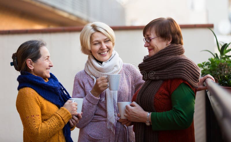 Two mature women drinking tea on a balcony and smiling. Two mature women drinking tea on a balcony and smiling