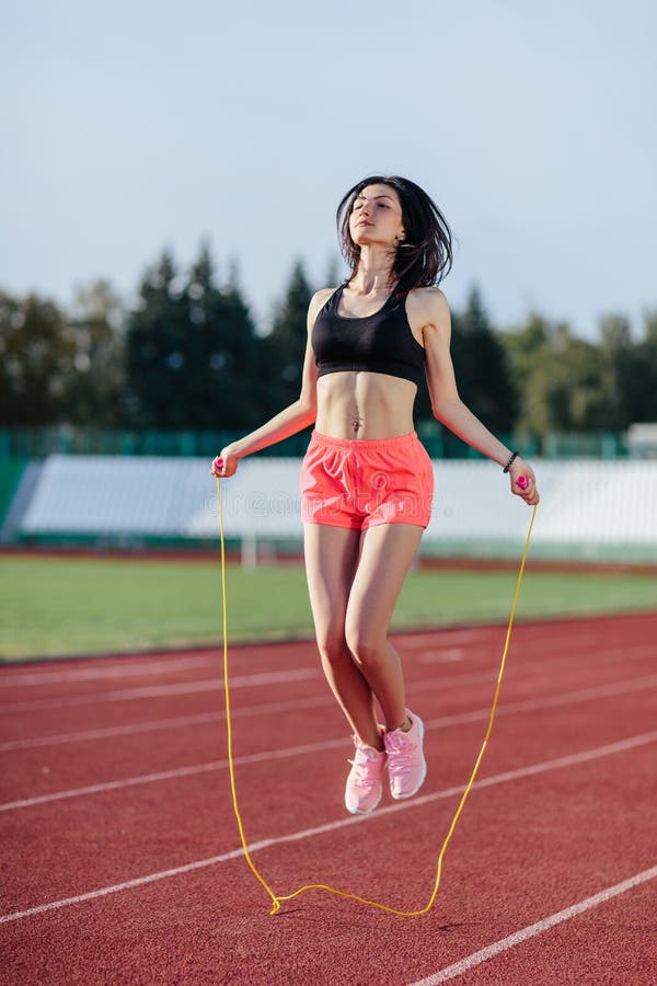 Dokonywa? best rezultaty Piękna młoda brunetki kobieta odziewa omijać linowy i uśmiechnięty w sportach podczas gdy ćwiczący na fotografia stock Dokonywa? best rezultaty Piękna młoda brunetki kobieta odziewa omijać linowy i uśmiechnięty w sportach podczas gdy ćwiczący na fotografia stock