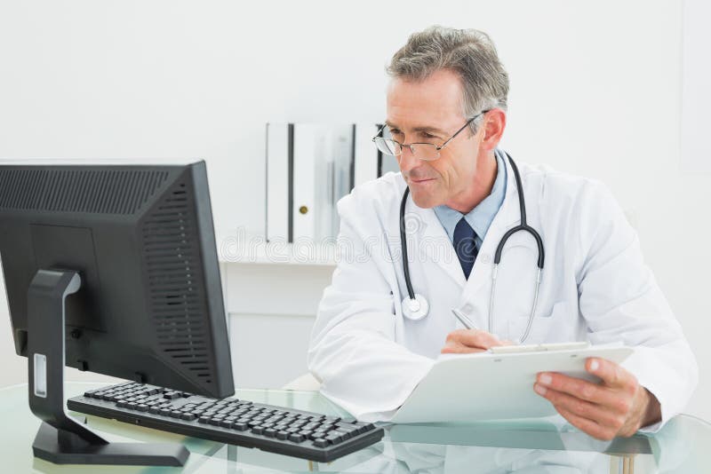 Doktor med rapporten som ser datorbildskärmen på det medicinska kontoret