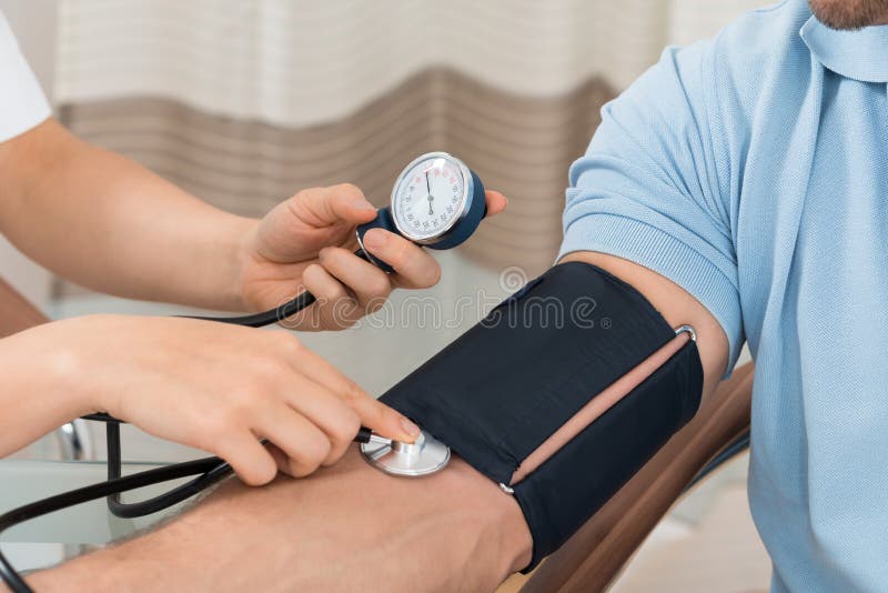 Doktor som mäter blodtryck av den manliga patienten royaltyfri bild Doktor som mäter blodtryck av den manliga patienten royaltyfri bild