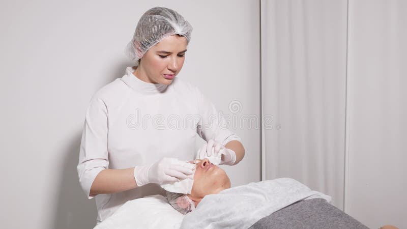 Doktorskosmetologen tar bort makeuppatienten som ligger på en special tabell