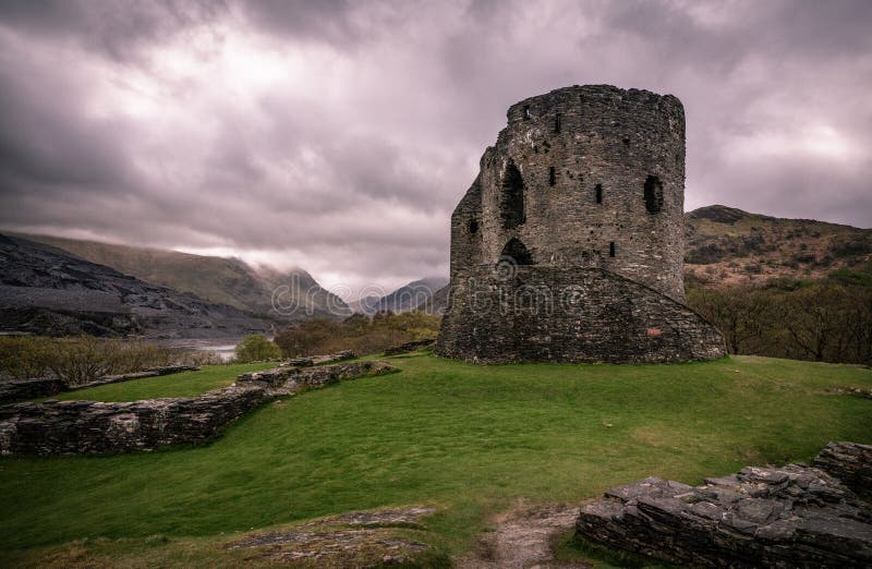 Welsh castle ruin on a hill, overlooking Snowdonia national park on a misty overcast day with dramatic clouds and green rocky hills. Welsh castle ruin on a hill, overlooking Snowdonia national park on a misty overcast day with dramatic clouds and green rocky hills.