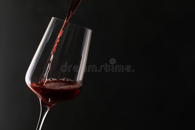 Pouring red wine into glass on dark background. Space for text. Pouring red wine into glass on dark background. Space for text