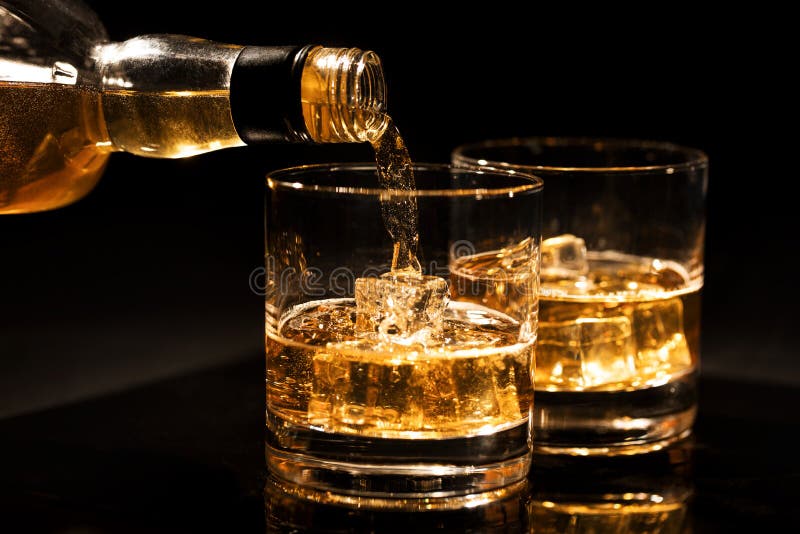 Pouring whiskey into a glass from bottle with ice cubes on black background. Pouring whiskey into a glass from bottle with ice cubes on black background