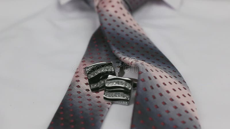 Dolly shot. Close-up knotted pink tie and cufflinks on a white shirt.