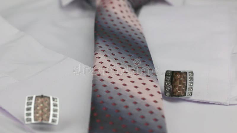 Dolly shot. Close-up knotted pink tie and cufflinks on a white shirt.