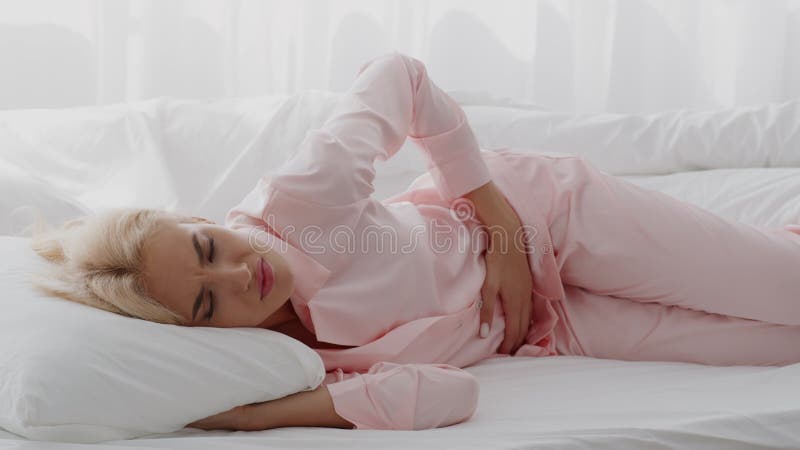 Dolor menstrual. mujer rubia enferma que toca el vientre mientras está en la cama almacen de video