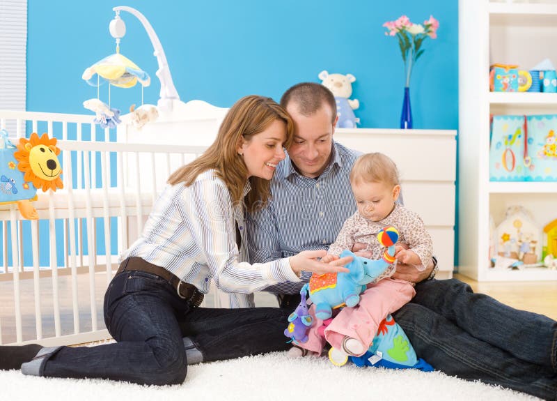 Happy family (father, mother and 1 year old baby girl) playing together at home, sitting on floor in children's room, smiling. Toys are officially property released. Happy family (father, mother and 1 year old baby girl) playing together at home, sitting on floor in children's room, smiling. Toys are officially property released.