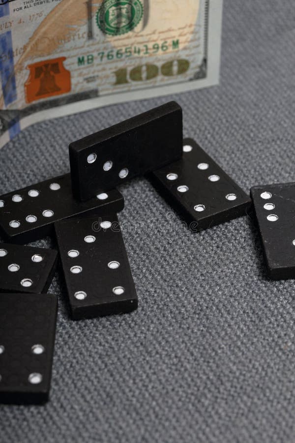 Domino knykcie na powierzchni zakrywającej z prostackim szarym płótnem W pobli?u jest sto dolarowych rachunk?w zdjęcie stock Domino knykcie na powierzchni zakrywającej z prostackim szarym płótnem W pobli?u jest sto dolarowych rachunk?w zdjęcie stock