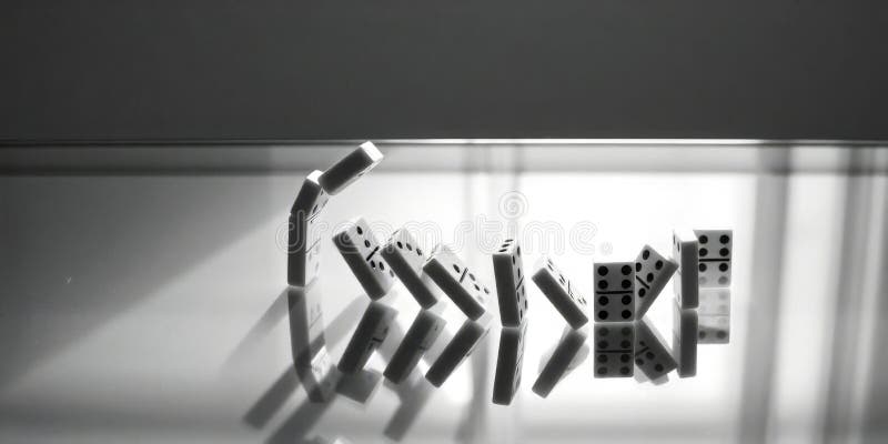 Dominoes falling in a creative arrangement on a reflective surface with shadows creating depth stock images