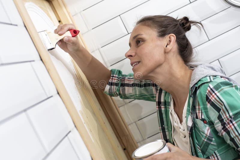 Domowa naprawa Uśmiechnięta piękna kobieta maluje drewnianego drzwi w łazience w bielu z muśnięciem