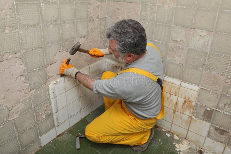 Adult worker remove, demolish old tiles in a bathroom with hammer and chisel. Adult worker remove, demolish old tiles in a bathroom with hammer and chisel