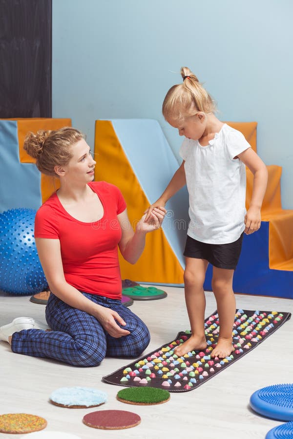 Shot of a girl holding her therapist's hand while she's walking on a sensory mat. Shot of a girl holding her therapist's hand while she's walking on a sensory mat