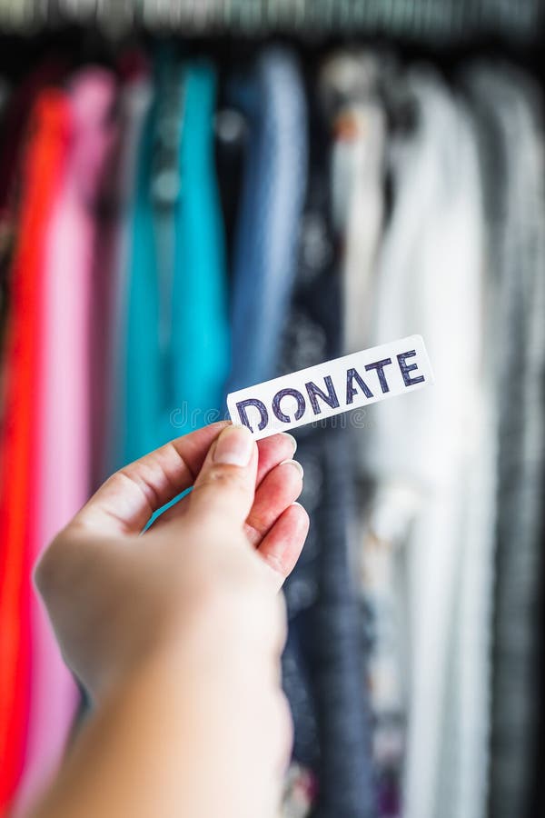 shopping and consumerism, Donate sign held in front of wardrobe full of clothes stock images