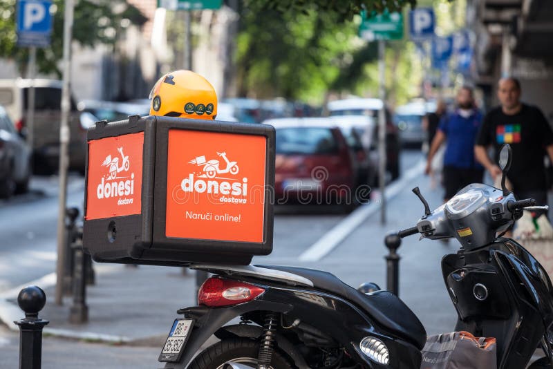 BELGRADE, SERBIA - AUGUST 22, 2020: ...Picture of a food delivery bag with the logo of Donesi Dostava on a delivery Scooter. Donesi is a service of Foodpanda a web platform part of the group, a German dot-com company specialized in online food ordering and. BELGRADE, SERBIA - AUGUST 22, 2020: ...Picture of a food delivery bag with the logo of Donesi Dostava on a delivery Scooter. Donesi is a service of Foodpanda a web platform part of the group, a German dot-com company specialized in online food ordering and