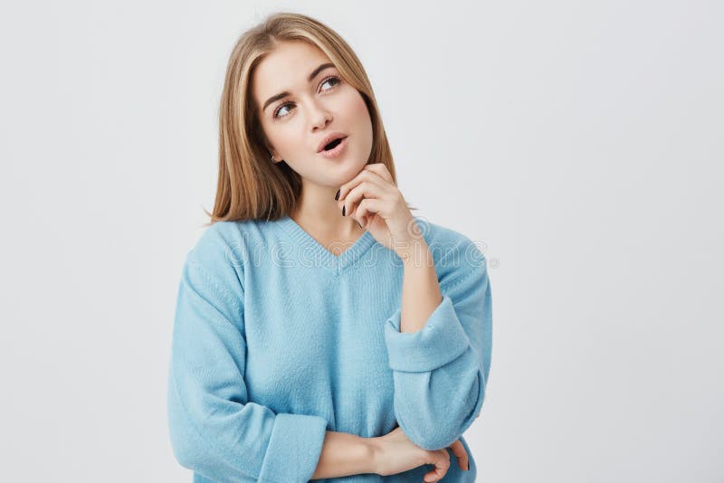 Donker-eyed jonge vrouw met eerlijk haar die blauwe sweater dragen die peinzende uitdrukking hebben die over haar plannen, het ki stock foto Donker-eyed jonge vrouw met eerlijk haar die blauwe sweater dragen die peinzende uitdrukking hebben die over haar plannen, het ki stock foto