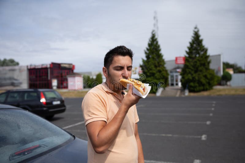 Donkerbruine mens die hotdog in het parkeren eten stock foto's Donkerbruine mens die hotdog in het parkeren eten stock foto's