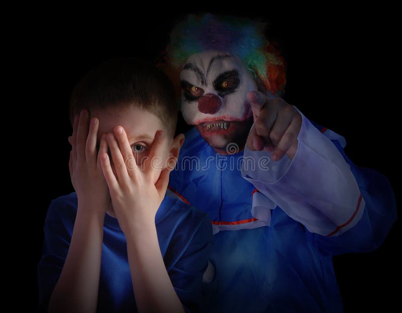 A child is hiding his eyes in the dark night and looks scared and upset at creepy clown. The boy is isolated on a black background for a fear concept. A child is hiding his eyes in the dark night and looks scared and upset at creepy clown. The boy is isolated on a black background for a fear concept.