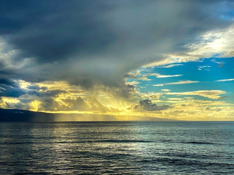 Clouds gather over open water of the Pacific Ocean off the coast of Maui, Hawaii. Sunset turns the sky golden yellow. Clouds gather over open water of the Pacific Ocean off the coast of Maui, Hawaii. Sunset turns the sky golden yellow.