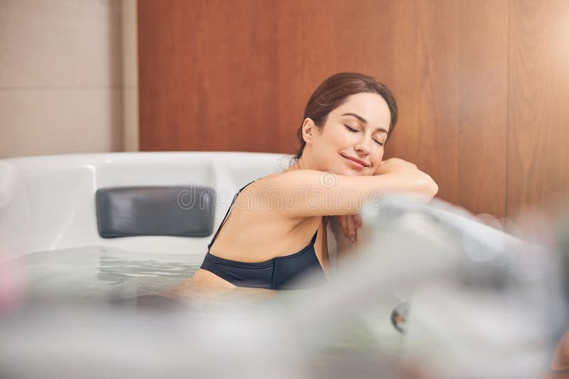 Attractive calm young modern Caucasian woman with her eyes shut relaxing in the hydromassage bathtub. Attractive calm young modern Caucasian woman with her eyes shut relaxing in the hydromassage bathtub