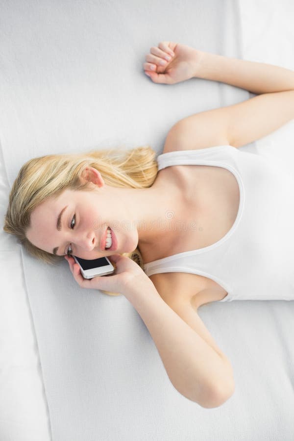 Donna abbastanza calma che si trova sul suo letto mentre telefonando con il suo smartp fotografia stock libera da diritti Donna abbastanza calma che si trova sul suo letto mentre telefonando con il suo smartp fotografia stock libera da diritti