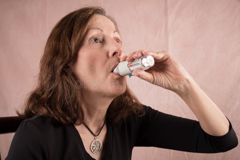 Donna adulta che per mezzo di un inalatore immagini stock Donna adulta che per mezzo di un inalatore immagini stock