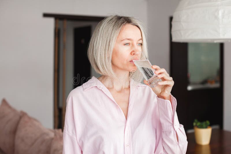 Donna adulta che tiene in casa un bicchiere di acqua minerale pura immagine stock libera da diritti