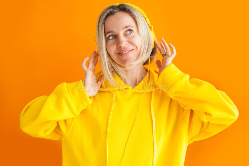 Donna adulta di cappuccio giallo e cuffie isolate sul muro giallo fotografia stock