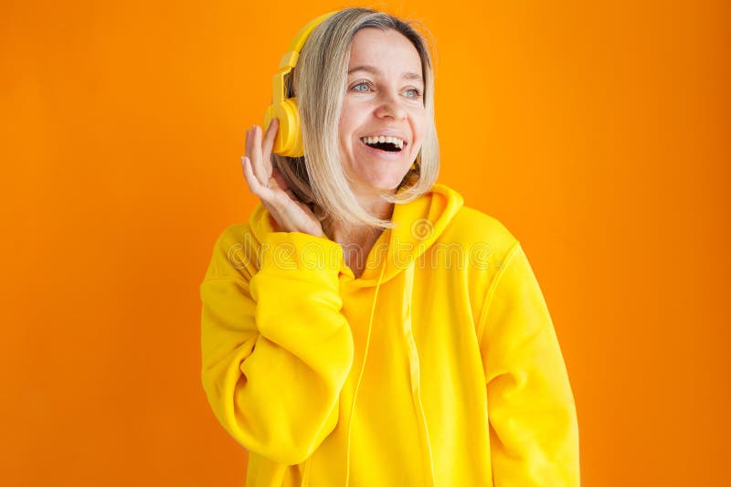 Donna adulta di cappuccio giallo e cuffie isolate sul muro giallo immagini stock