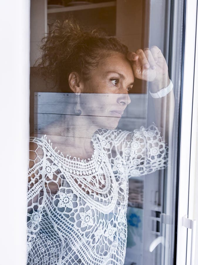 Donna adulta triste che si trova in casa e guarda fuori attraverso il vetro della finestra della porta. concetto di esaurimento me fotografia stock