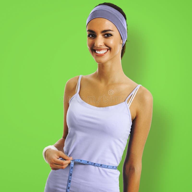 Woman in sportswear measuring waist with a tape measure, on green color background. Sporty african american girl at studio. Health, dieting and fitness gym center concept. Square composition. Woman in sportswear measuring waist with a tape measure, on green color background. Sporty african american girl at studio. Health, dieting and fitness gym center concept. Square composition