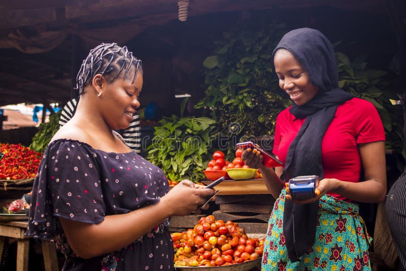 Donna africana che fa acquisti di cibo in un mercato locale pagando facendo un trasferimento via telefono per un commerciante