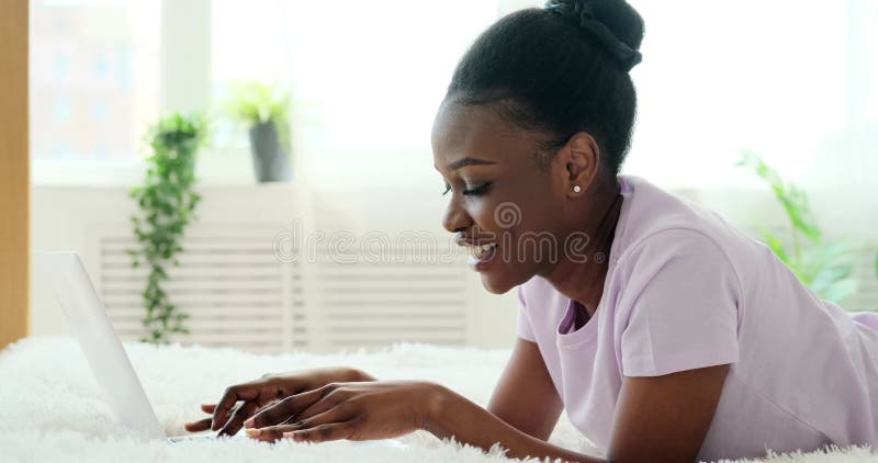 Donna afro-americana felice che scrive sul computer portatile a letto stock footage