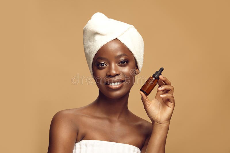 Donna afro-americana positiva dopo le procedure spa usando siero facciale. Donna afro-americana positiva dopo le procedure di spa utilizzando siero facciale in una fiala di vetro marrone con berretto nero su beige. cosmetici organici naturali imballaggi di prodotti di bellezza ecocompatibili.