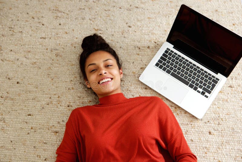 Donna afroamericana che si trova sul tappeto con il computer portatile fotografie stock libere da diritti Donna afroamericana che si trova sul tappeto con il computer portatile fotografie stock libere da diritti