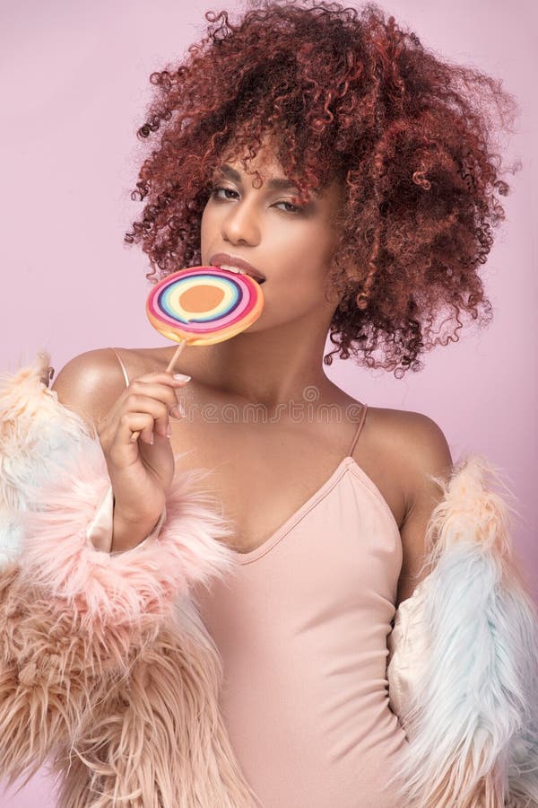 Donna alla moda di afro con la lecca-lecca su fondo rosa fotografia stock Donna alla moda di afro con la lecca-lecca su fondo rosa fotografia stock