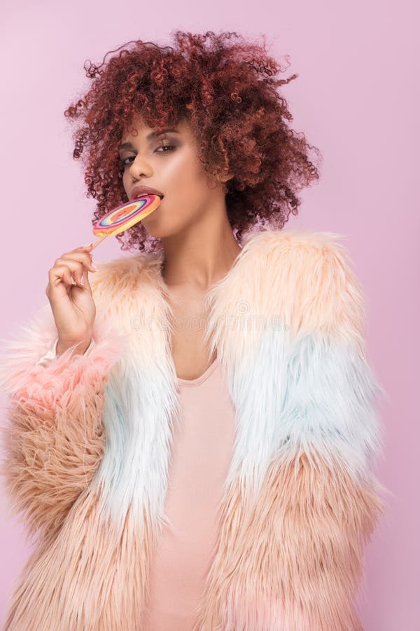 Donna alla moda di afro con la lecca-lecca su fondo rosa fotografia stock libera da diritti Donna alla moda di afro con la lecca-lecca su fondo rosa fotografia stock libera da diritti