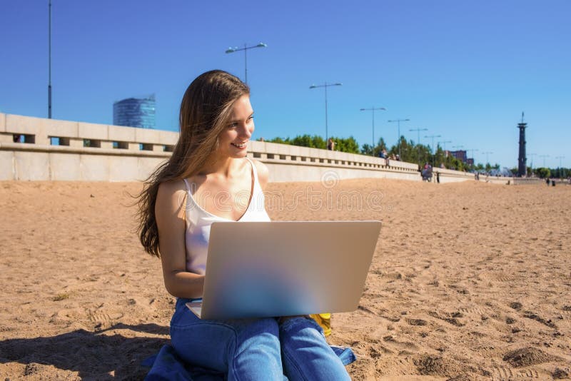 Happy smiling hipster girl skilled freelance copywriter enjoying good sunny summer day during distance work on laptop computer, sitting on the beach. Happy smiling hipster girl skilled freelance copywriter enjoying good sunny summer day during distance work on laptop computer, sitting on the beach.