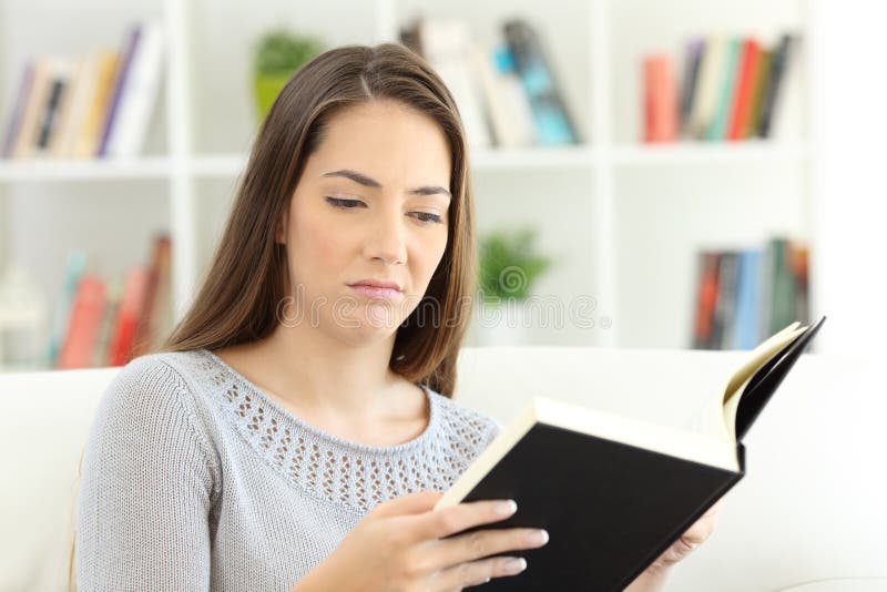 Bored woman reading a bad book sitting on a sofa at home. Bored woman reading a bad book sitting on a sofa at home