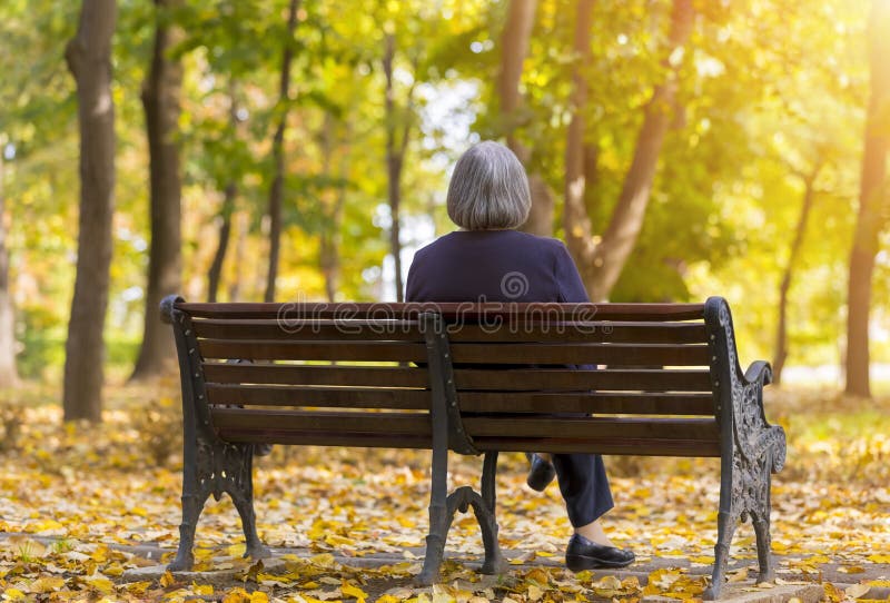 Donna anziana che si siede su un banco nel parco di autunno fotografie stock libere da diritti Donna anziana che si siede su un banco nel parco di autunno fotografie stock libere da diritti