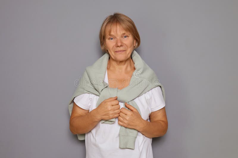 Donna anziana con camicia bianca e saltella sul collo sorridendo allegra e soddisfatta guardando la telecamera con il viso calmo fotografia stock