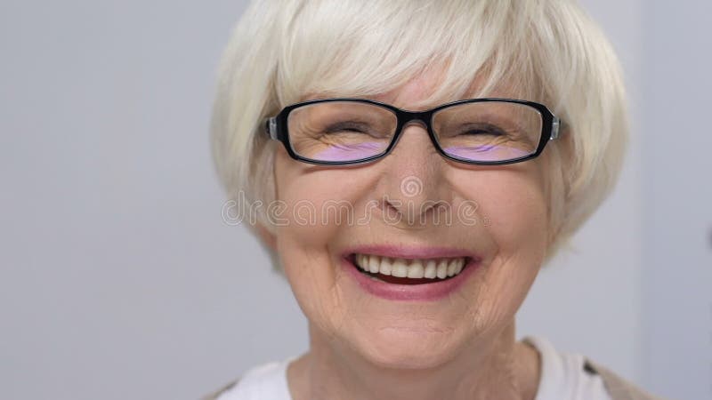 Donna anziana con occhiali da sole che sorride felicemente alla telecamera, alla sanità, all'esame