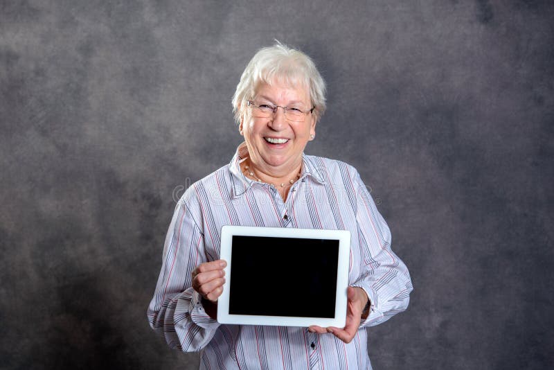 Donna anziana pelosa grigia amichevole che mostra il pc della compressa fotografia stock