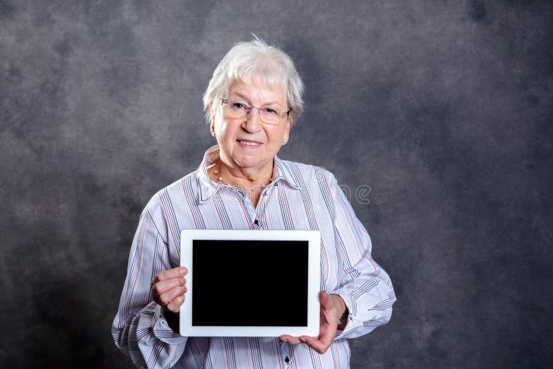 Donna anziana pelosa grigia che per mezzo del pc della compressa immagine stock