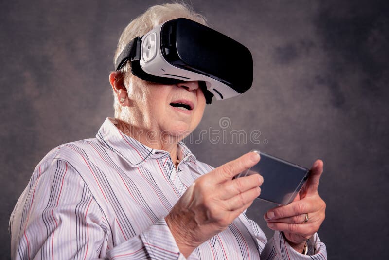 Donna anziana pelosa grigia che usando i vetri di realtà virtuale immagine stock